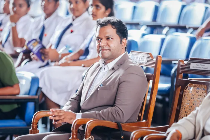 A guest seated in the front row, listening, with students in the rows behind.