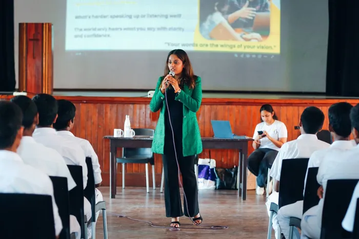 A speaker addressing the hall, with a slide behind reading that your words are the wings of your vision.
