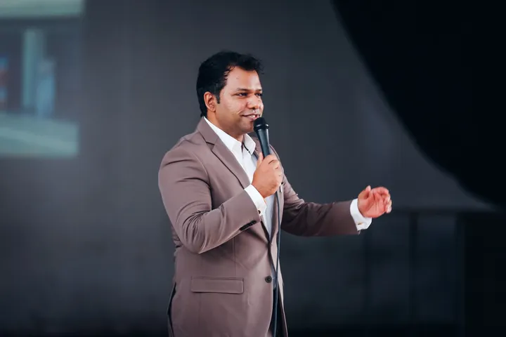 A speaker on stage, mid-sentence, microphone in hand.